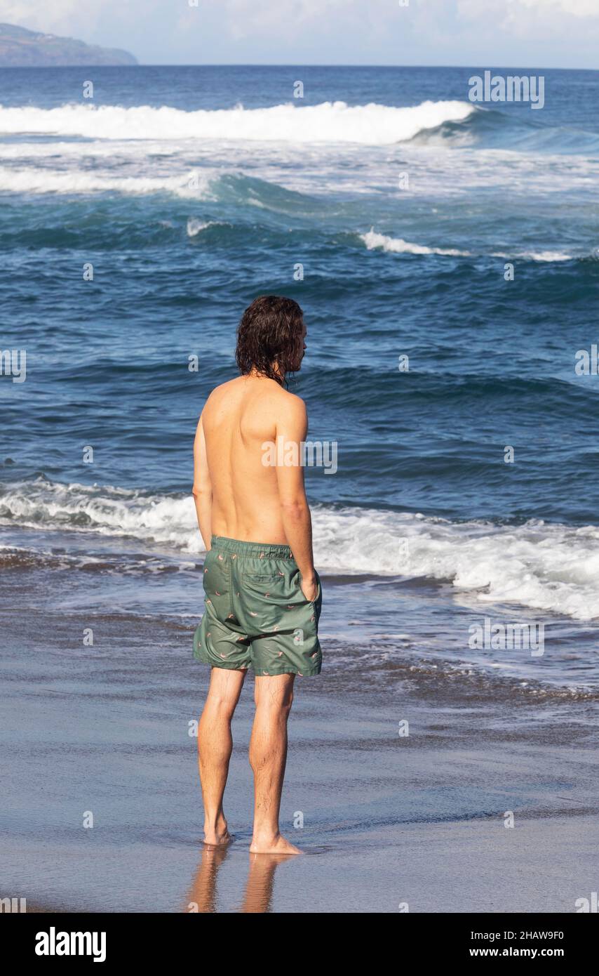 Junger Mann, der im Meer am Strand von Praia de Santa Barbara, Ribeira Grande, Sao Miguel Island, Azoren, Portugal, steht Stockfoto