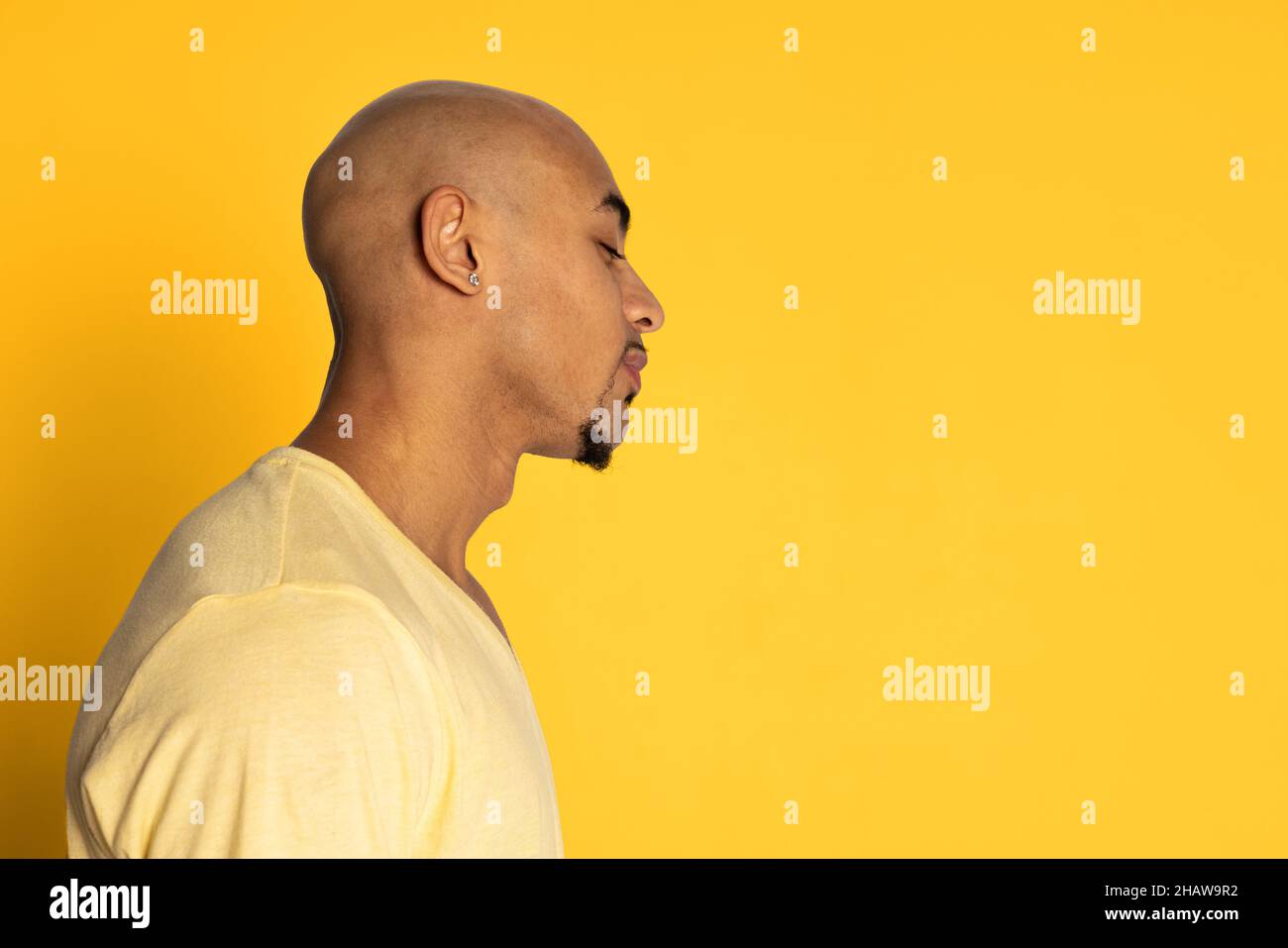 Profilansicht eines dunkelhäutigen kahlen Mannes im T-Shirt, der gerade isoliert auf gelbem Studiohintergrund aussieht. Konzept der menschlichen Emotionen Stockfoto