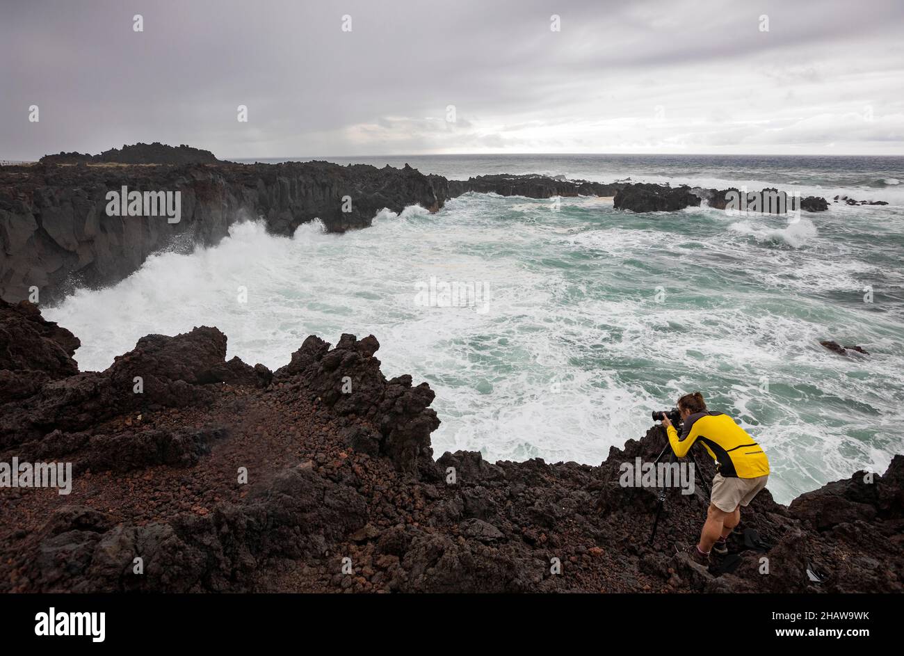 Fotograf auf der vulkanischen Klippe bei Flut mit hohen Wellen, Ponta da Ferraria, Sao Miguel Island, Azoren, Portugal Stockfoto