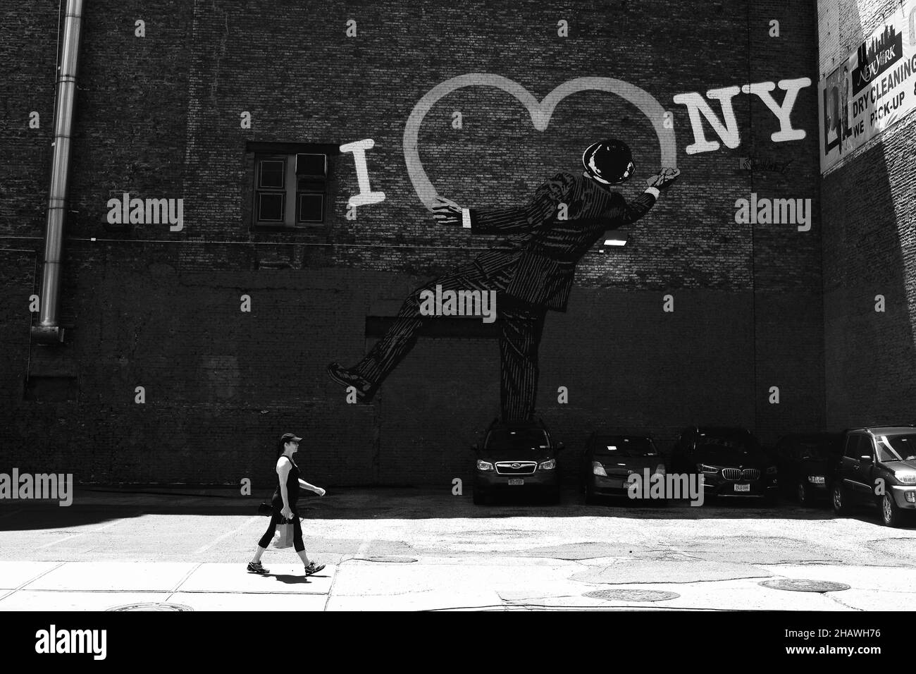 NEW YORK, USA - 02. März 2021: Eine Graustufe einer Frau, die mit Autos an einer Straße entlang läuft und ein Graffiti mit dem Titel „I love NY“ im Hintergrund in New York Stockfoto