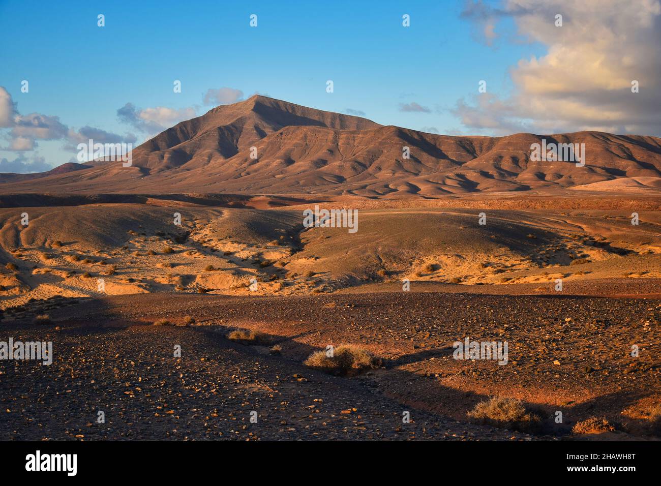 Costa de Papagayo in Lanzarote, Spanien. Die Bergkette Los Ajaches bei Sonnenuntergang. Ein sonniger Abend mit einigen Wolken am blauen Himmel, goldene Stunde. Stockfoto