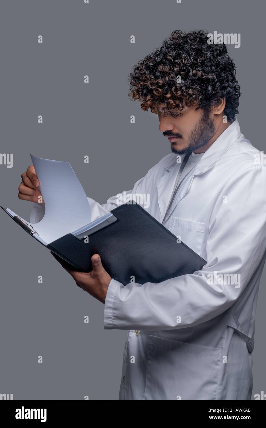 Konzentrierter indischer Arzt mit lockigen Haaren prüft Dokumente Stockfoto