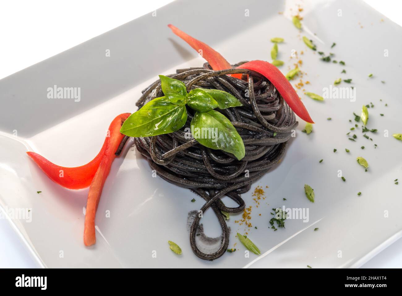Spaghetti mit schwarzer Tintenfisch-Tinte - italienische Pasta al nero di seppia mit Basilikumblättern - aus der Nähe in einer weißen Schale isoliert auf Weiß Stockfoto