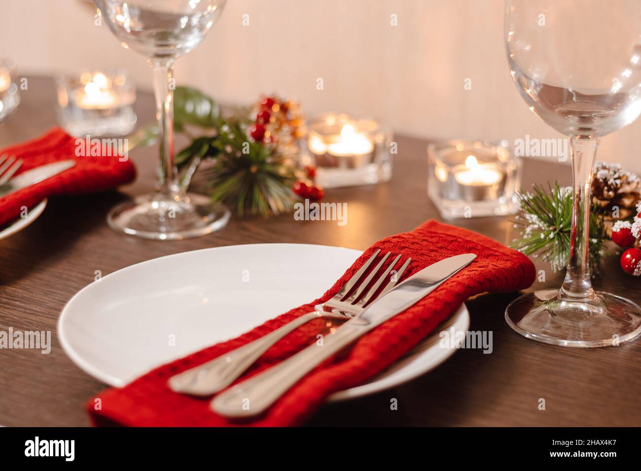 Weihnachtliche Tischeinstellung. Teller und Besteck auf Serviette. Vorbereitung auf das festliche Abendessen. Kerzen brennen am Heiligabend auf dem Tisch. Stockfoto