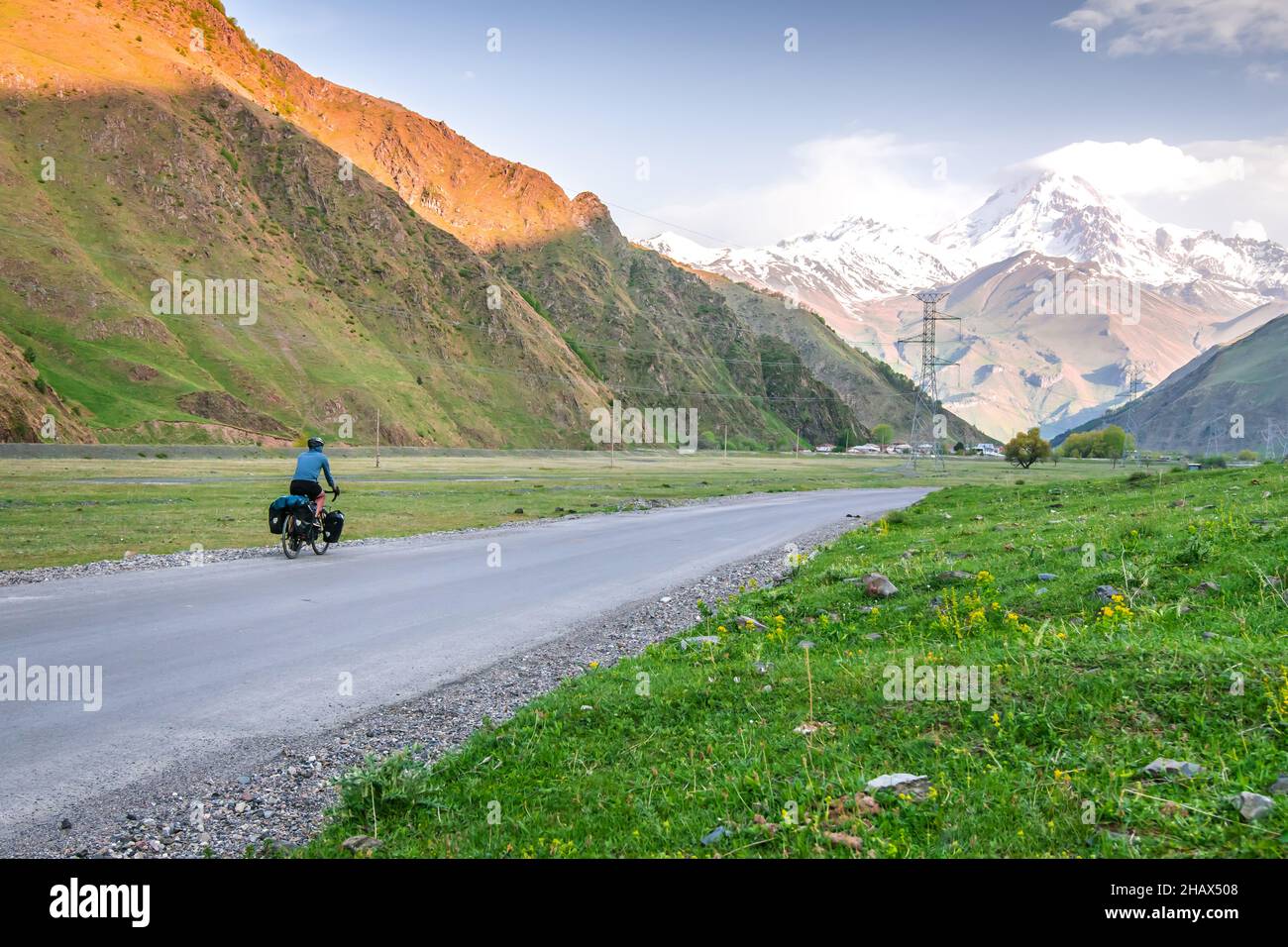 Männliche Person in blauer Jacke Radfahren mit Tourenrad umgeben von Bergen und grünen Sommer nture. Tou rund um den kazbegi Nationalpark. Stockfoto