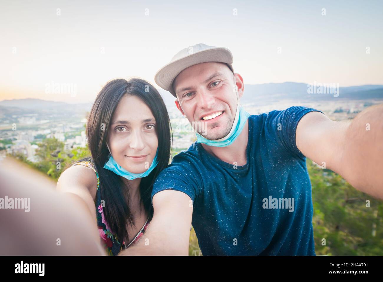 Nahaufnahme von männlichen und weiblichen Gesichtern mit Masken, während ein Selfie-Handheld mit Panoramablick auf die Stadt im Hintergrund aufgenommen wird. Neuer Normalwert Stockfoto