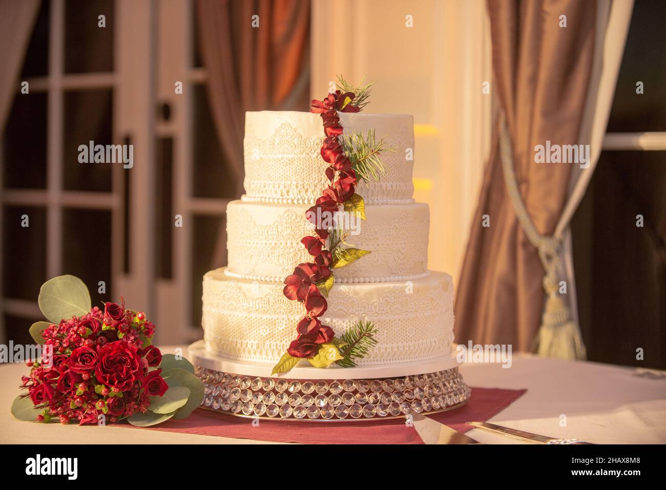 Wunderschöne dreistufige weiße Hochzeitstorte mit roten Blumen Dekoration beim Hochzeitsempfang Stockfoto