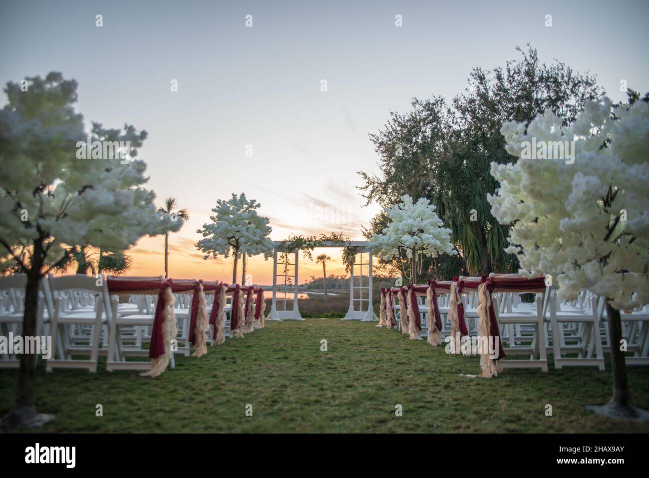Weiße Hochzeitsstühle in Insel mit roten Schleifen und Bändern Stockfoto