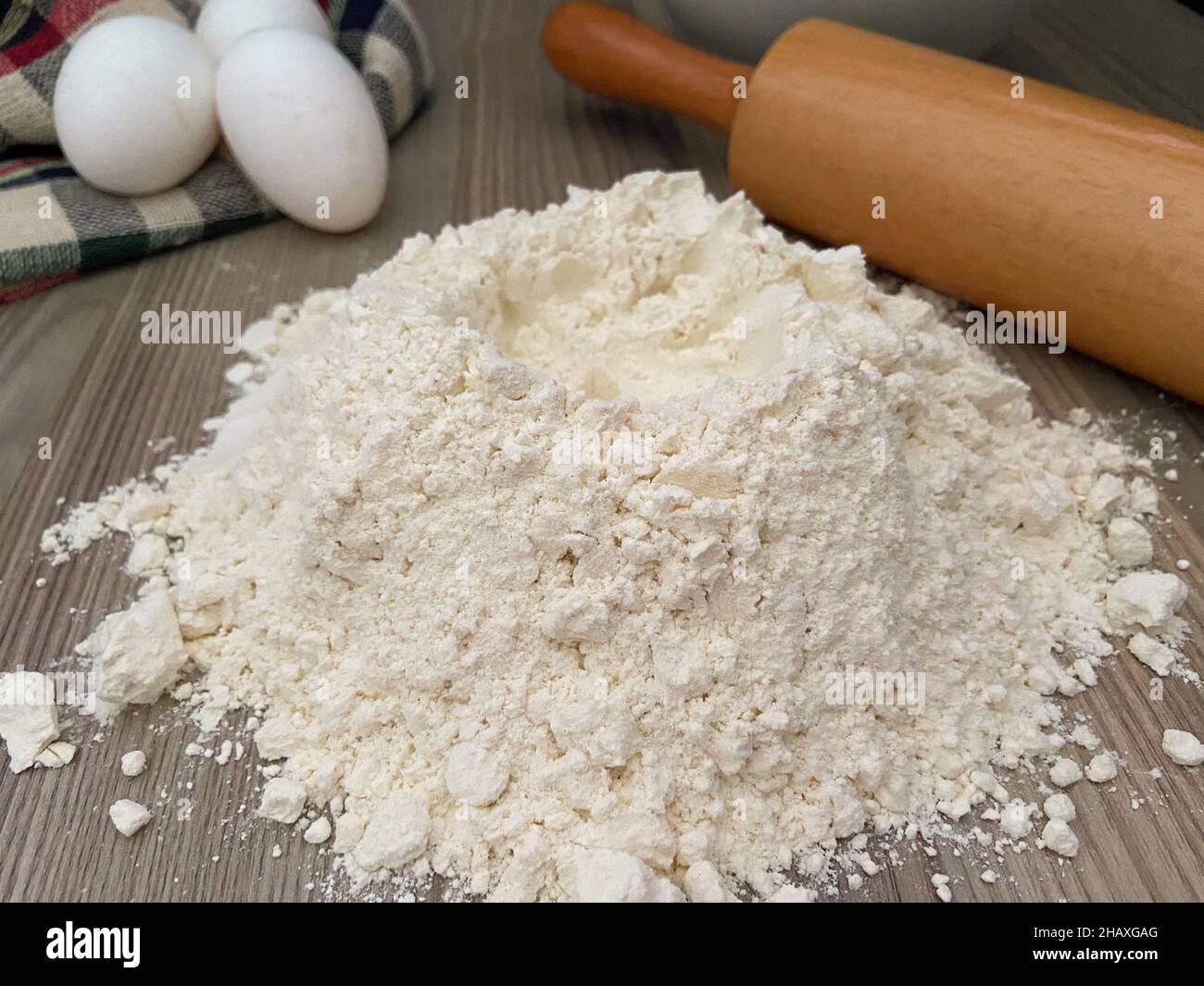 Weißes Mehl, farina auf dem Tisch mit dickem Nudelholz. Bäckereikonzept und Idee. Selektiver Fokus auf Mehl. Eier sind nicht zielgerichtet. Stockfoto