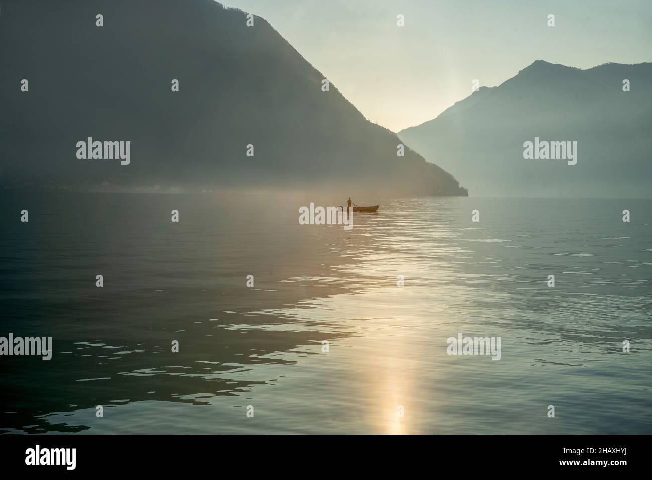 Neblige Landschaft auf dem Comer See mit Boot des Fischers und kleinem Körper der Silhouette des Fischers in der Ferne im Winter in Norditalien. Kaum sichtbar ho Stockfoto