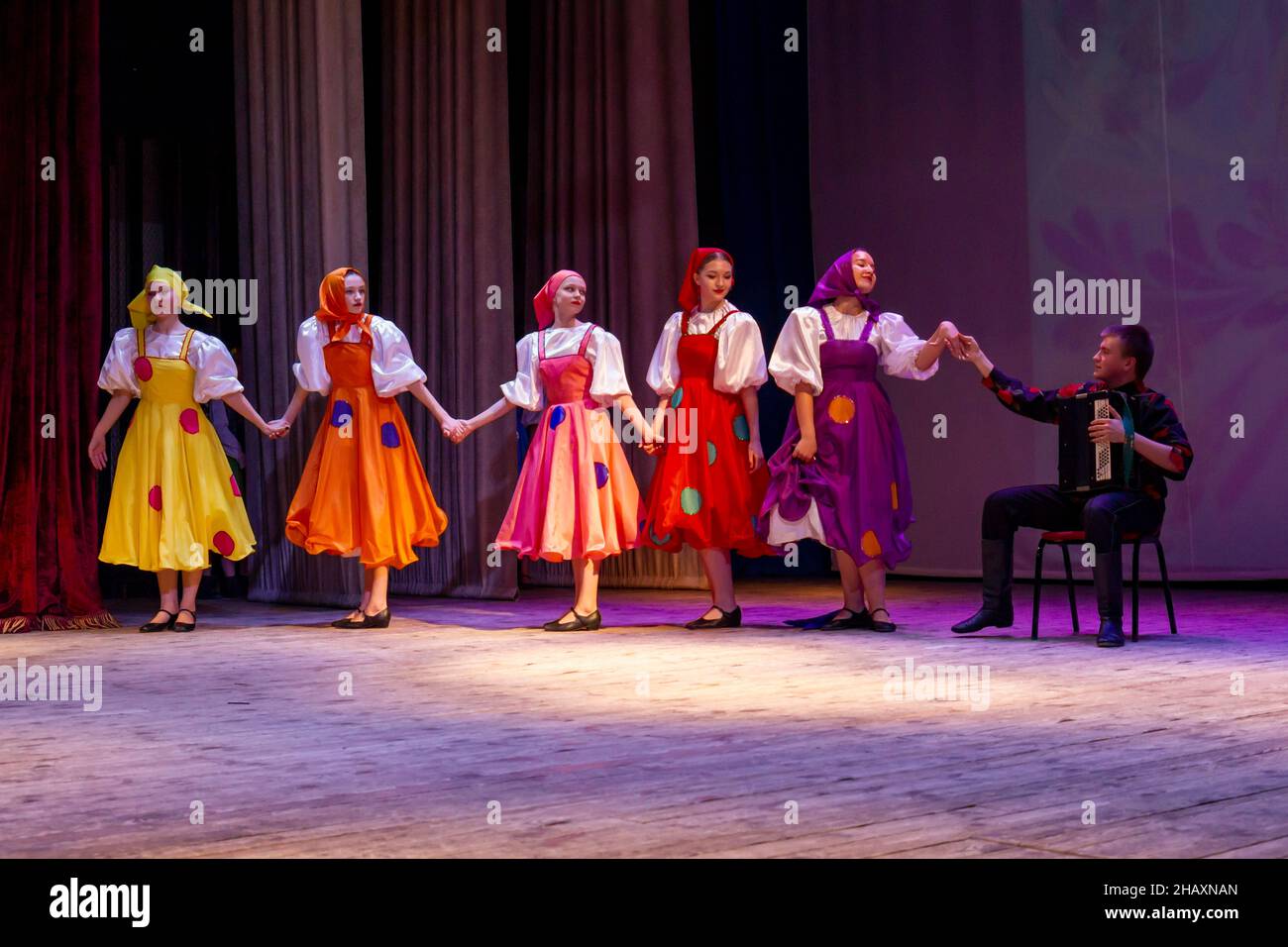 Omsk, Russland. 05. Dezember 2021. Bayan-Spieler und fünf Mädchen-Tänzer beenden den Prohodka-Tanz. Aufführung des Ensembles Samotsvety. Stockfoto