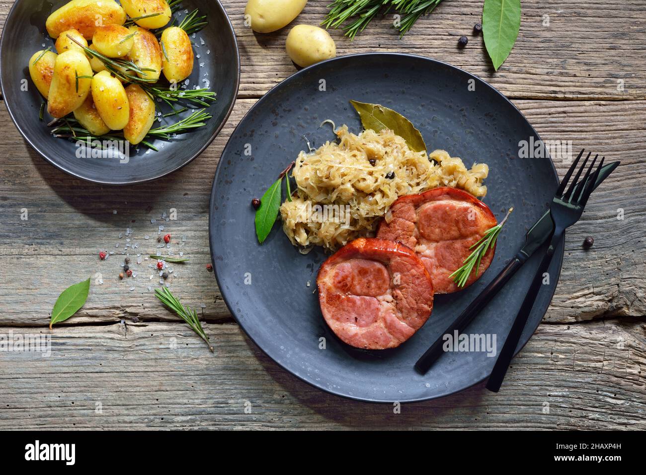 Deutsche Küche – geräucherter Schweinehalk mit Sauerkraut und gebratenen Babykartoffeln auf einem Keramikteller auf einem alten Holztisch Stockfoto