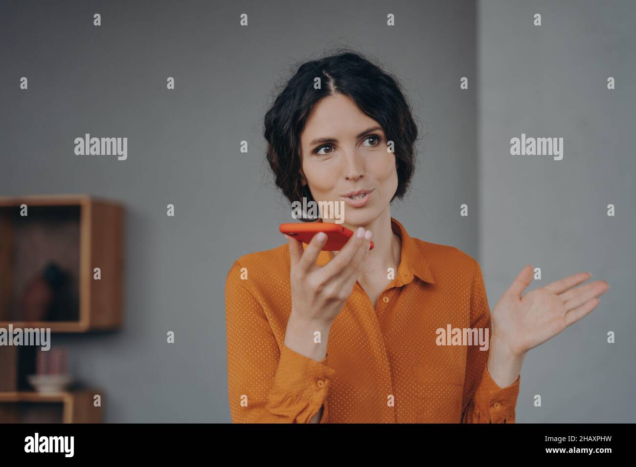 Schöne Brünette italienische Geschäftsfrau spricht elegant auf Lautsprecher auf Handy zu Hause Stockfoto