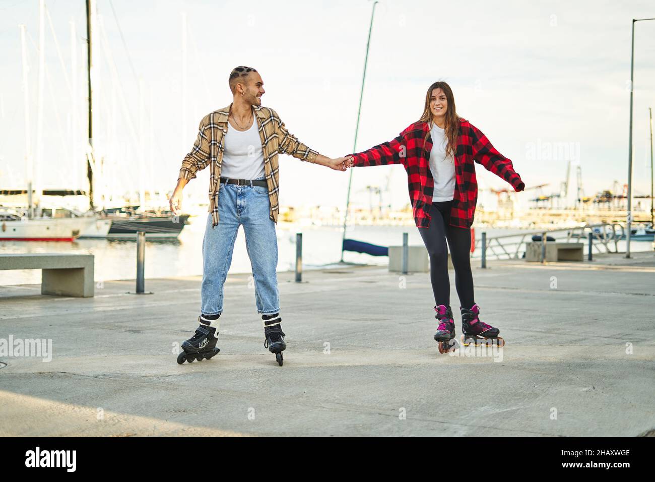 Ein ganzer Körper positiver junger Freunde, die sich an Rollschullaufbahnen halten und bei Sonnenuntergang eine angenehme gemeinsame Freizeit am Meer genießen Stockfoto