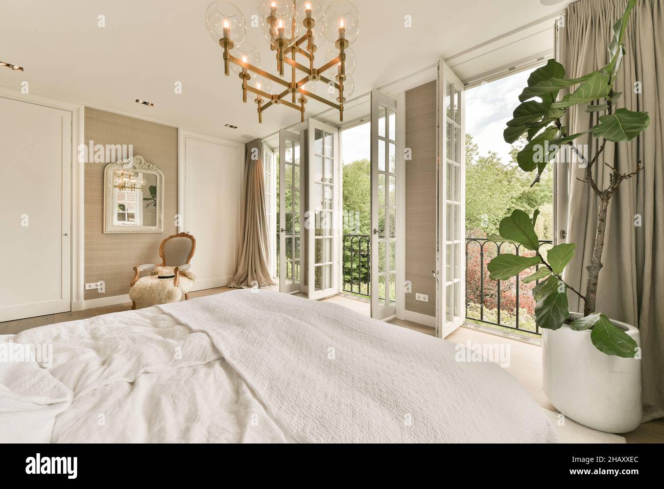 Komfortables Schlafzimmer in Pastelltönen mit großen Fenstern, die sich öffnen lassen, mit beigen Vorhängen, Retro-Sessel mit karierten, großen Betten, die mit Deckeln und überzogen sind Stockfoto