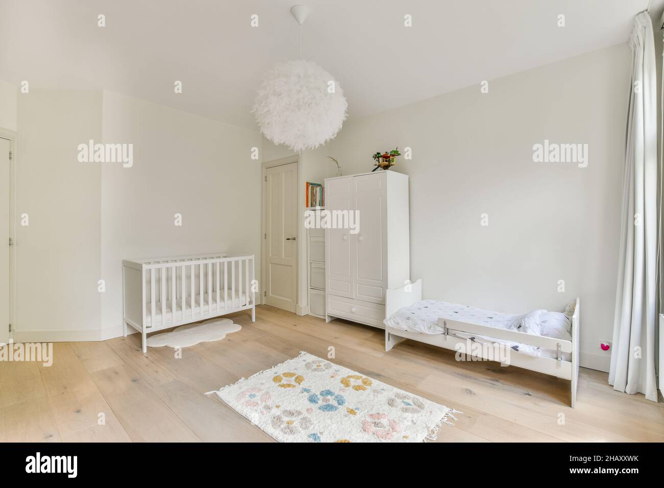 Kinderbett und Babybett in hellen geräumigen Schlafzimmer und Schrank in  der Nähe der weißen geschlossenen Tür in stilvollen Wohnung platziert  Stockfotografie - Alamy