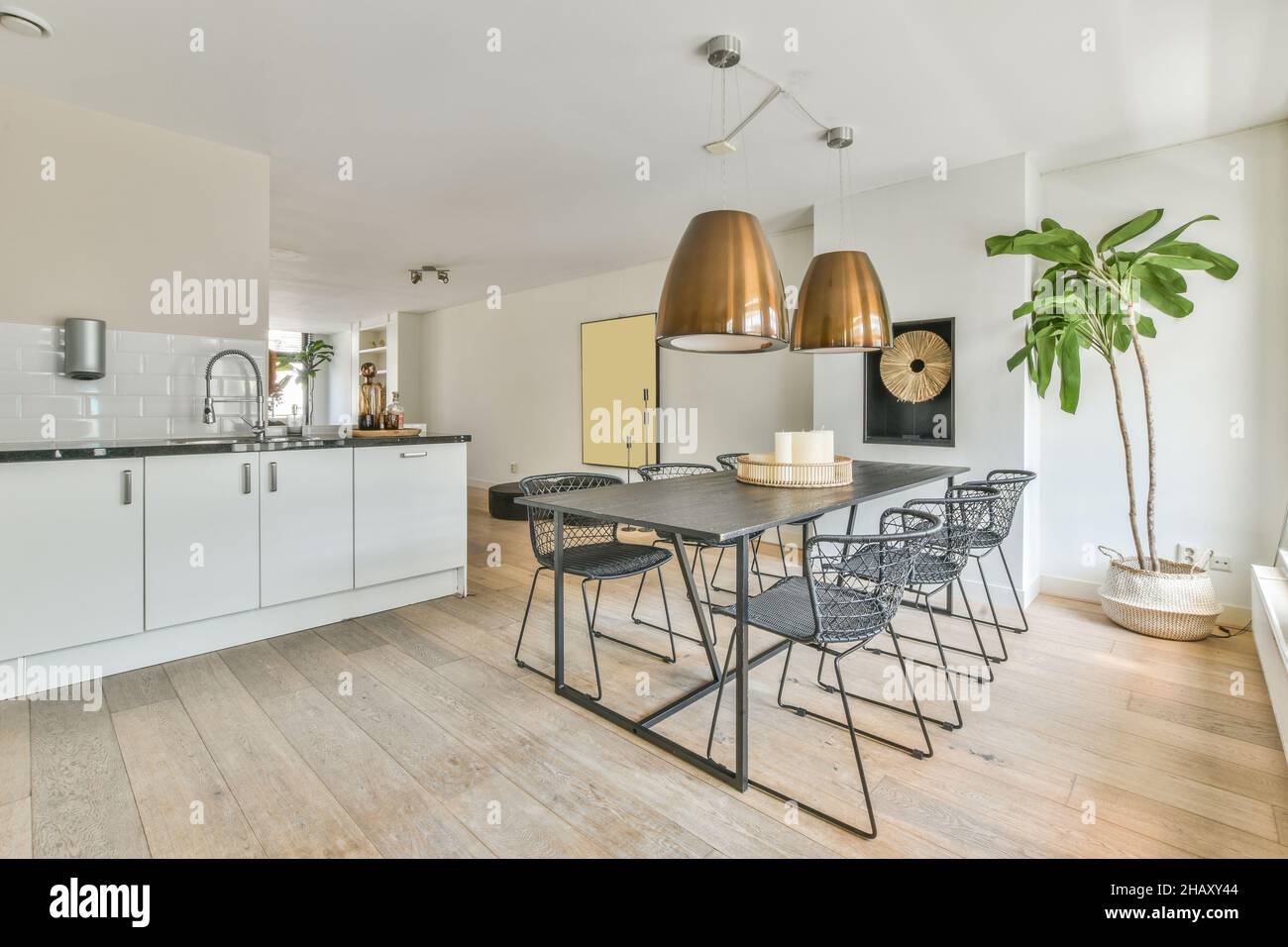 Stühle am Esstisch unter Lampen in heller Küche mit weißen Schränken und modernen Geräten in der Nähe von Fenstern in der Wohnung platziert Stockfoto