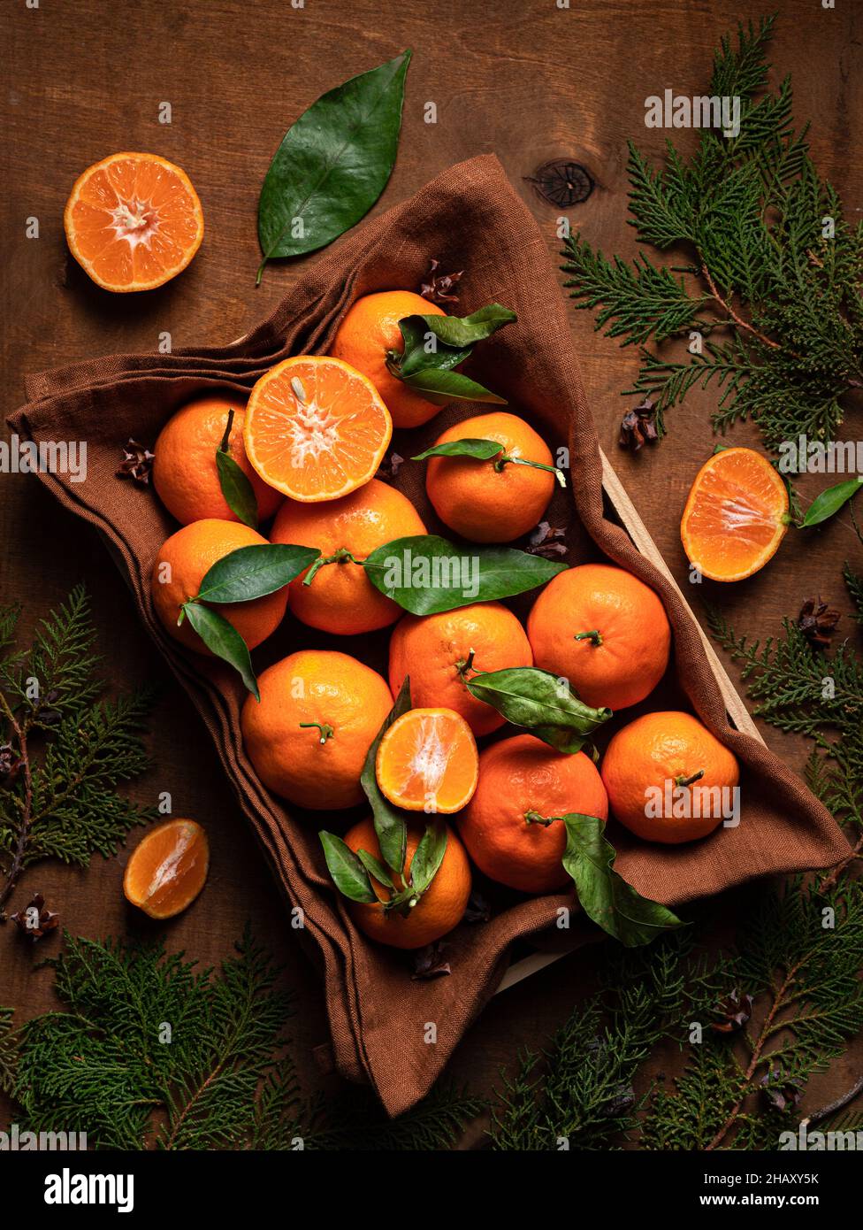 Draufsicht Haufen von frischen orange Mandarine mit Blättern in Behälter mit Textil auf Tisch mit grünen Zweigen im Raum platziert Stockfoto