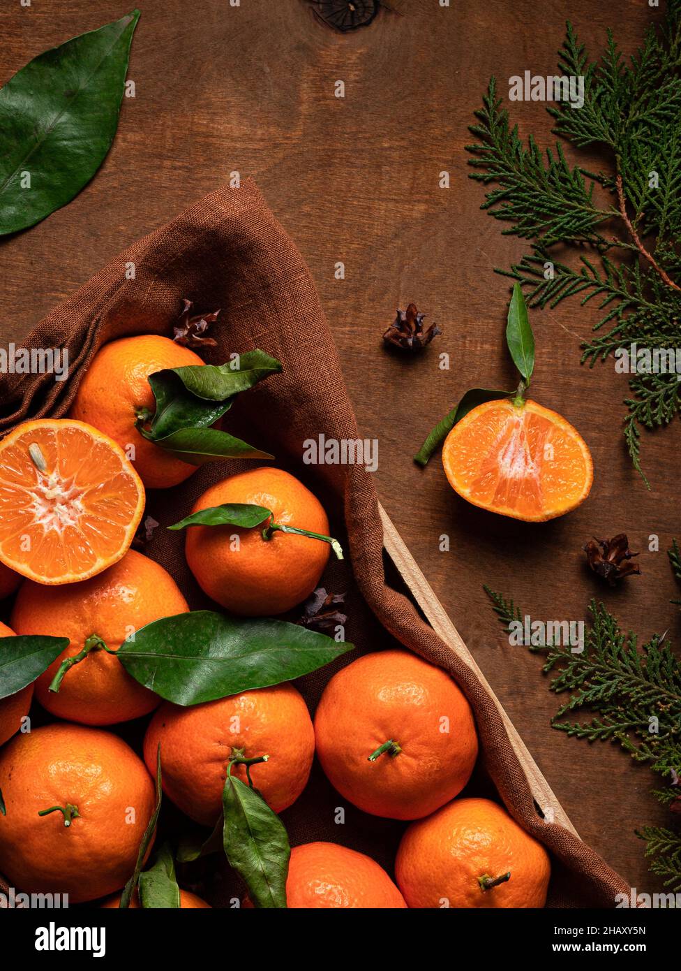 Draufsicht Haufen von frischen orange Mandarine mit Blättern in Behälter mit Textil auf Tisch mit grünen Zweigen im Raum platziert Stockfoto