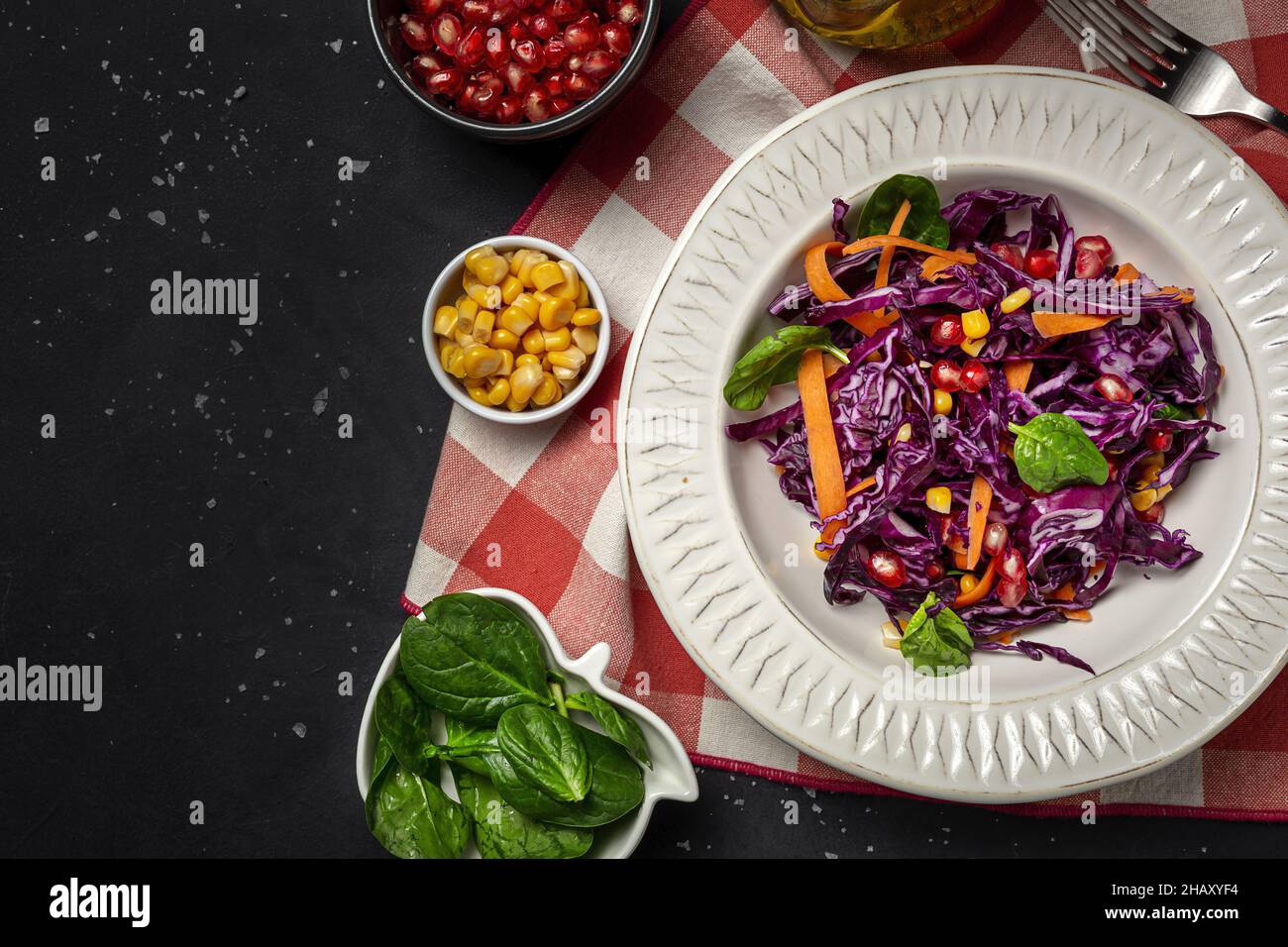 Hausgemachter purpurner Kohlsalat mit Mais, Karotten, Granatapfel und Spinat auf dunklem Grund. Veganes Lebensmittelkonzept. Gesunde Ernährung Stockfoto