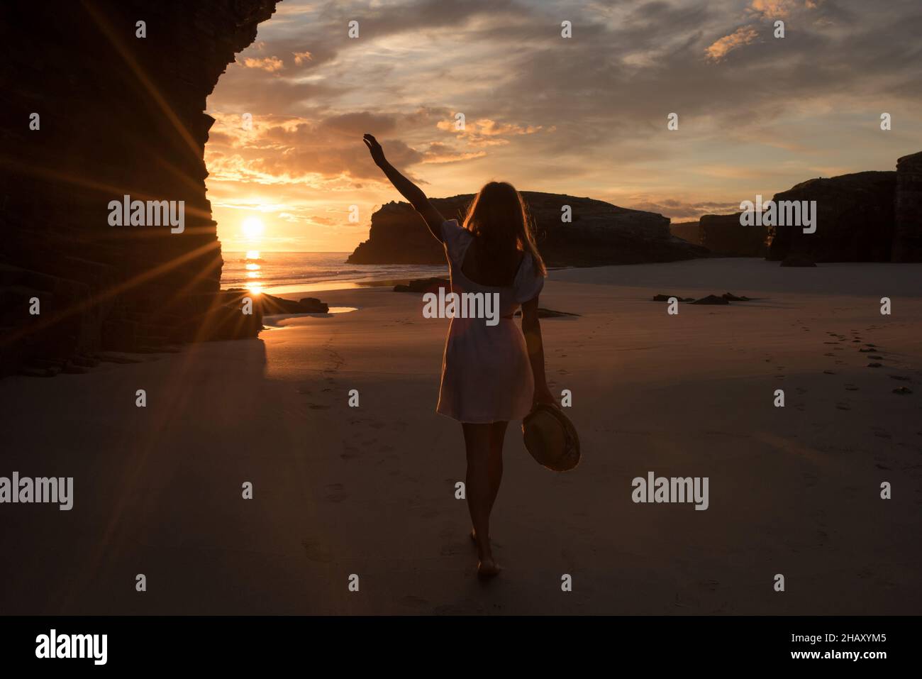 Silhouette einer einsamen, nicht erkennbaren Frau, die am Sandstrand der Kathedralen in der Nähe von felsigen Klippen steht und den malerischen Sonnenuntergang am Himmel bewundert Stockfoto