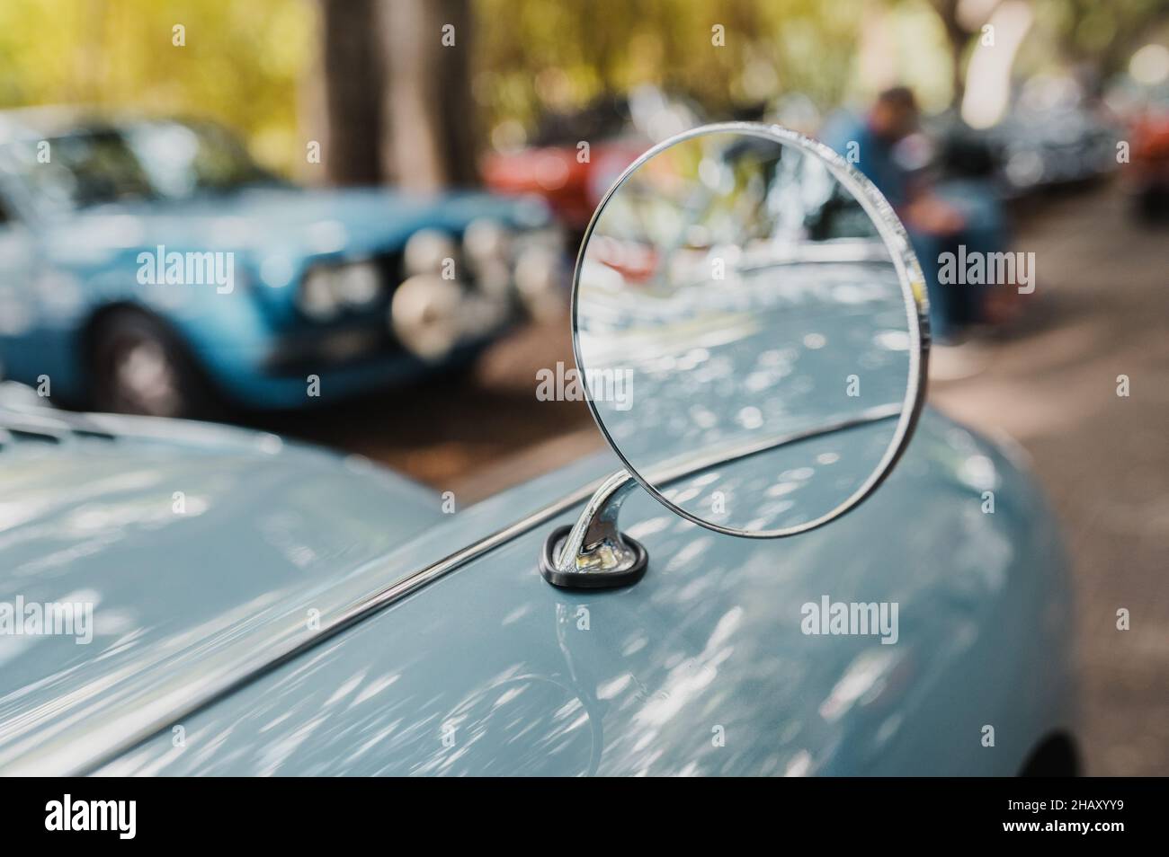 Runder Spiegel auf blauem Stoßfänger des alten Zeitfahrzeuges, das auf der Straße der Stadt in der Nähe verschiedener Autos auf verschwommenem Hintergrund geparkt wurde Stockfoto