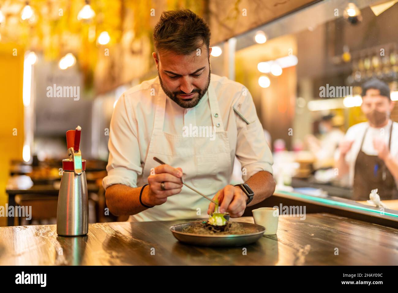 Bärtiger, professioneller Chefkoch, der Zutaten für Seeigel auf dem Teller am Tisch im modernen Restaurant zubereitet Stockfoto