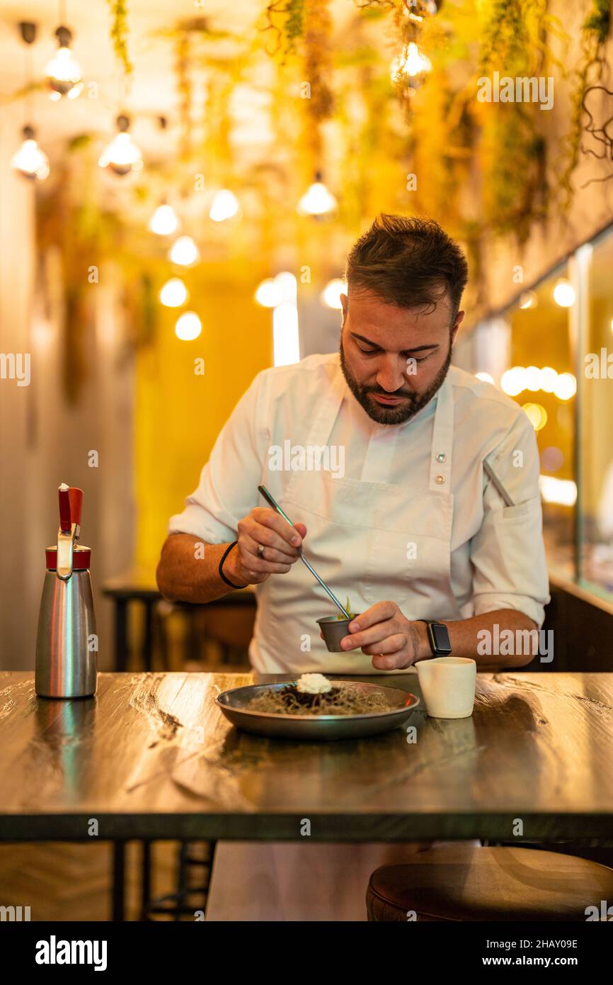 Bärtiger, professioneller Chefkoch, der Zutaten für Seeigel auf dem Teller am Tisch im modernen Restaurant zubereitet Stockfoto