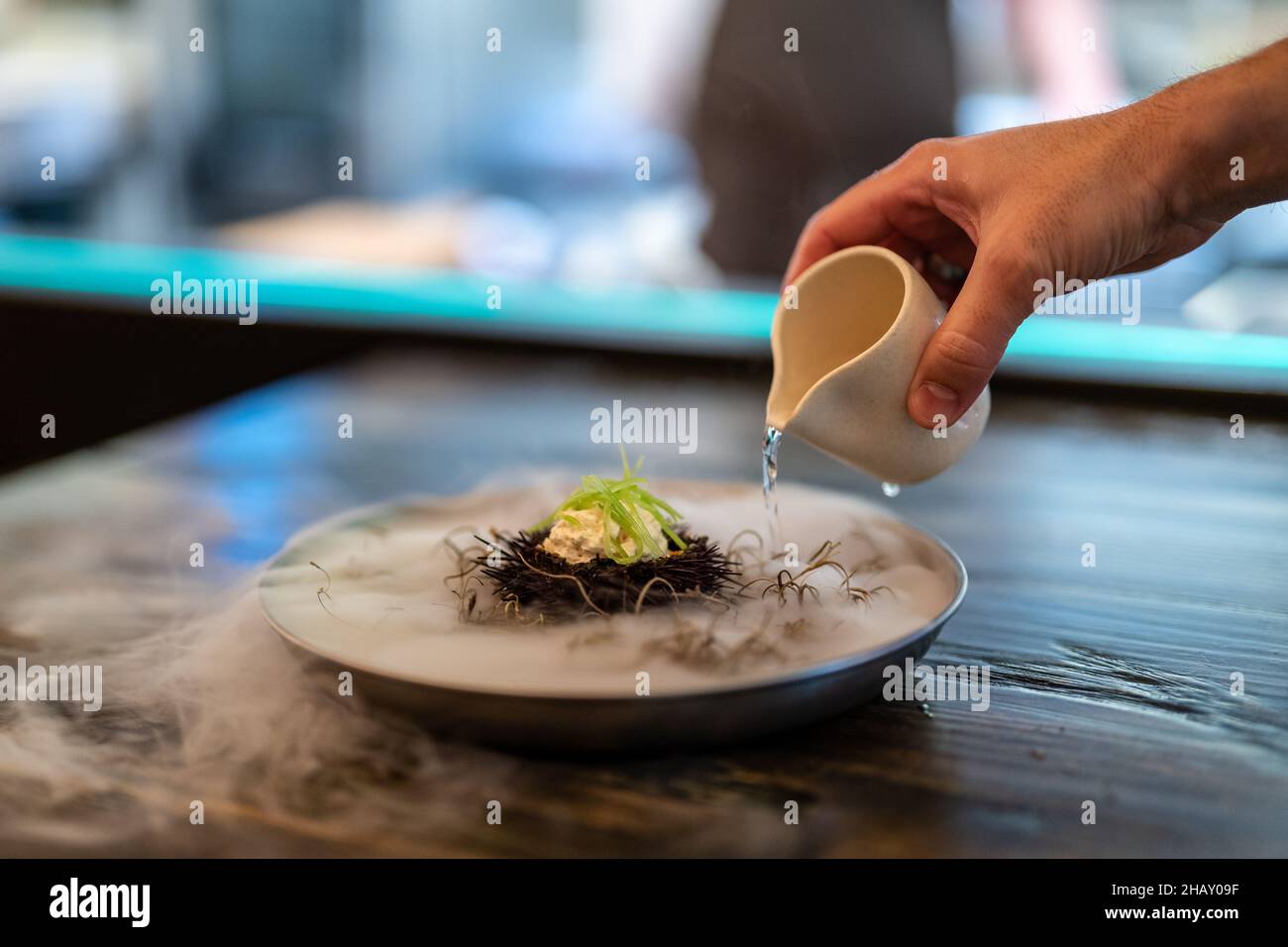 Crop anonyme Mann Gießen flüssigen Stickstoff aus Soße Boot auf Teller mit Seeigel in Molecular Cuisine Restaurant Stockfoto