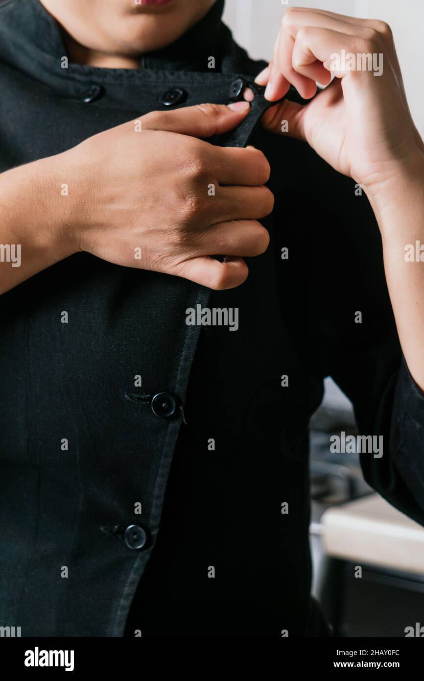 Während der Arbeit in einem modernen Restaurant knöpfte eine anonyme Frau die schwarze Jacke aus Chefuniform auf Stockfoto