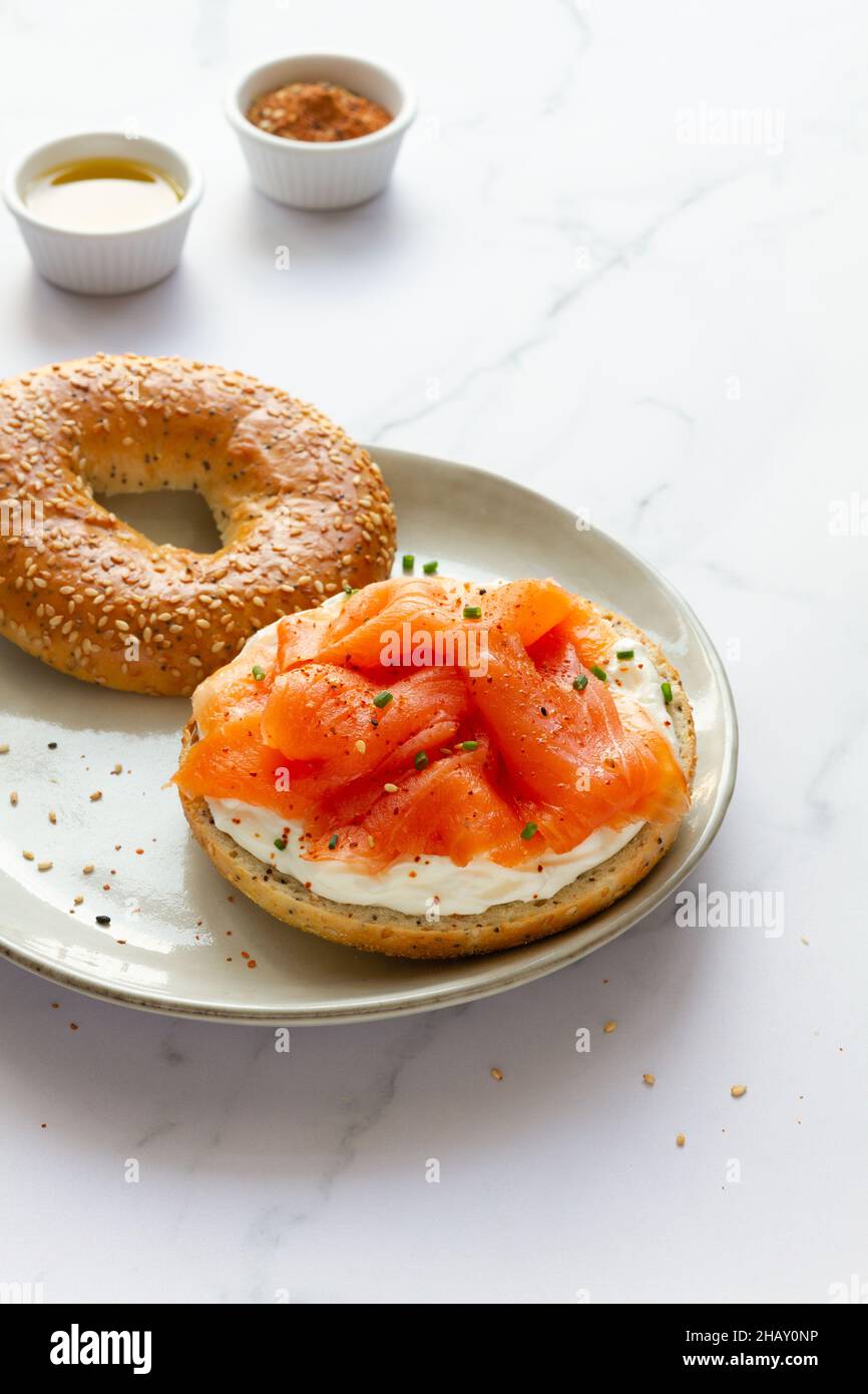 Frischer Bagel mit Käse und Lachs auf dem Teller serviert auf dem Tisch mit einer Tasse heißen Kaffee in der hellen Küche Stockfoto