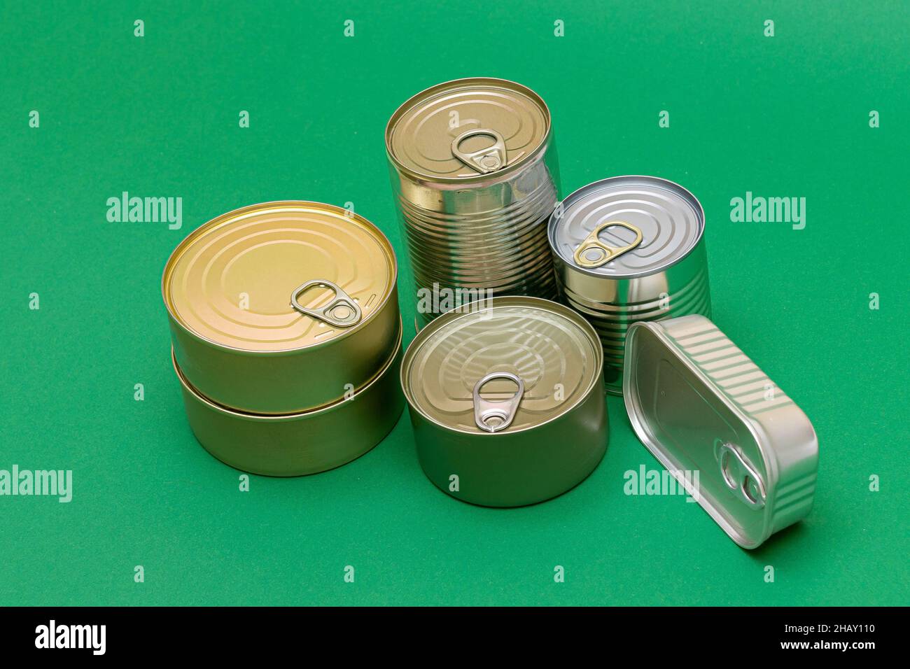 Eine Gruppe gestapelter Blechdosen mit leeren Kanten auf grünem Hintergrund. Konserven. Verschiedene Aluminiumdosen für die sichere und langfristige Lagerung von Lebensmitteln. Versiegelte Lebensmittelbehälter Aus Stahl Stockfoto