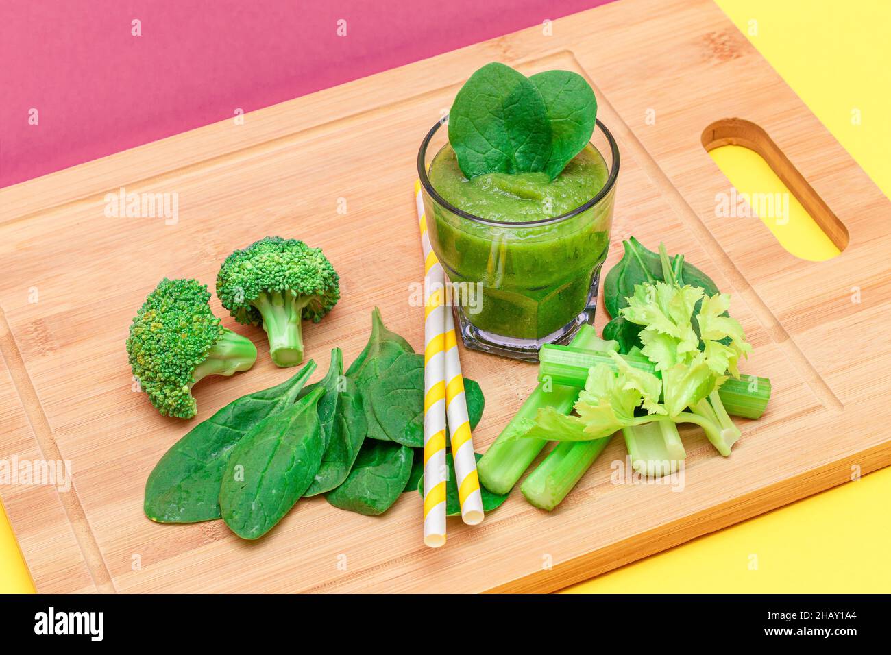 Frischer grüner Smoothie von Apfel, Sellerie und Spinat in Glasbecher mit gelbem Cocktailstroh auf Holzschneidebrett. Veganer Detox-Drink. Vegetarische Kultur. Gesunde Ernährung und Obst-Diät Stockfoto