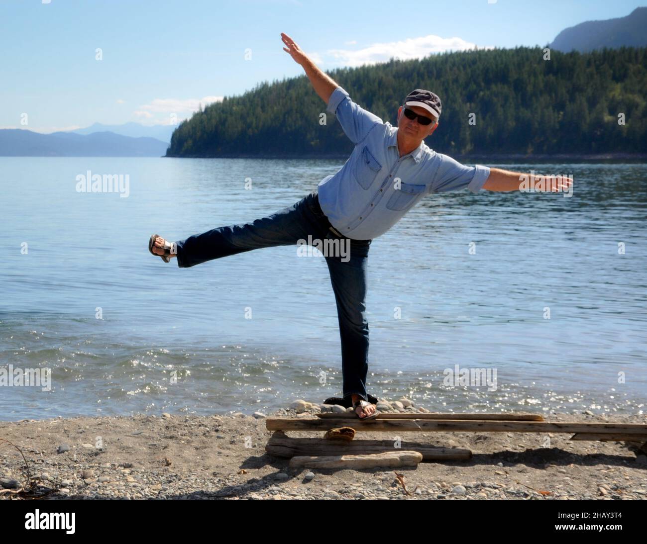 Mann, der auf einem Stück Holz am Strand steht und auf einem Bein balanciert, Kaslo, Kootenay Lake, British Columbia, Kanada Stockfoto