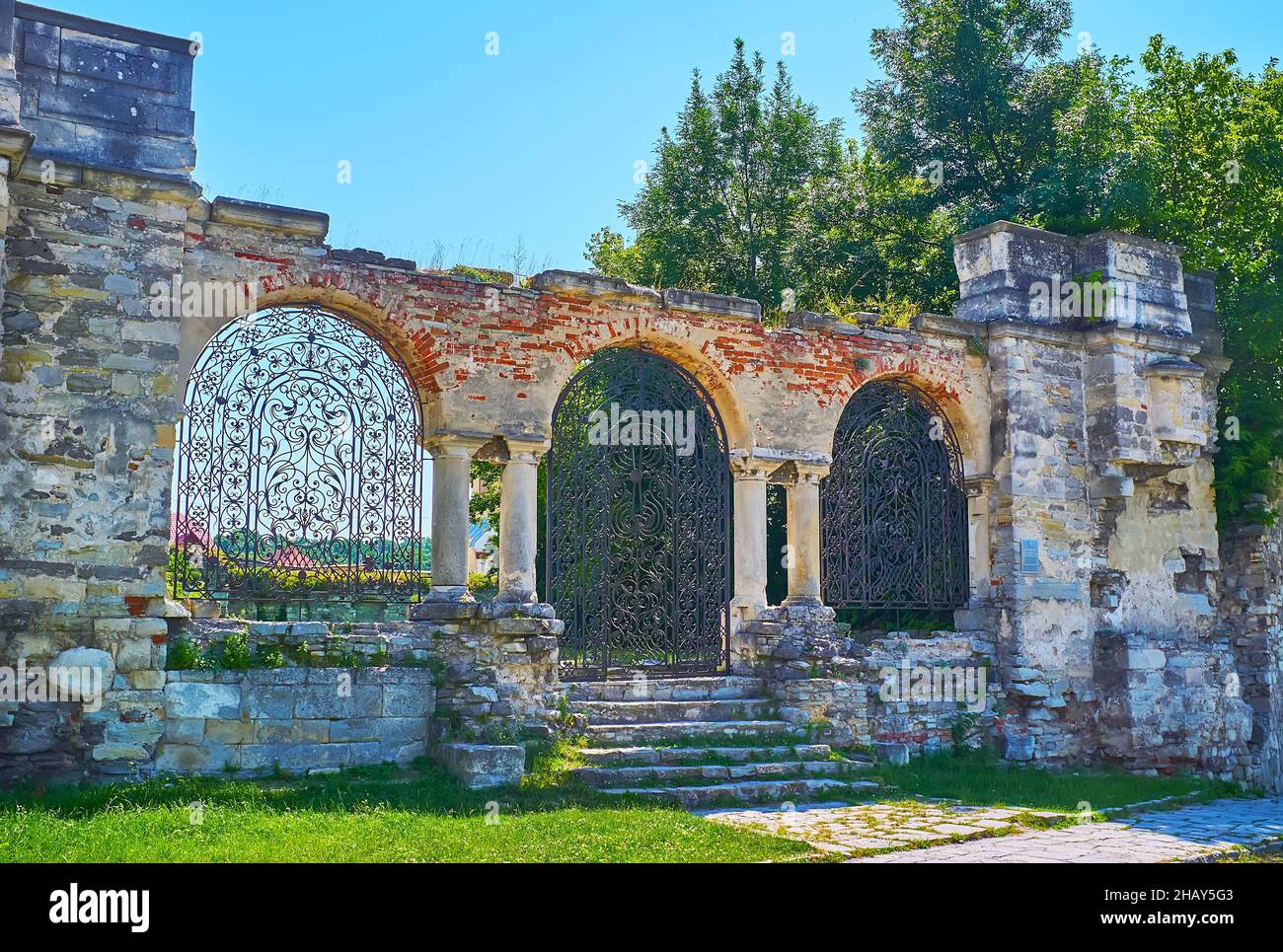 Das gewölbte Tor mit ornamentalem gusseisernem Gitter führt zum Ort der ruinierten armenischen Nikolaikirche, Kamianets-Podilskyi, Ukraine Stockfoto