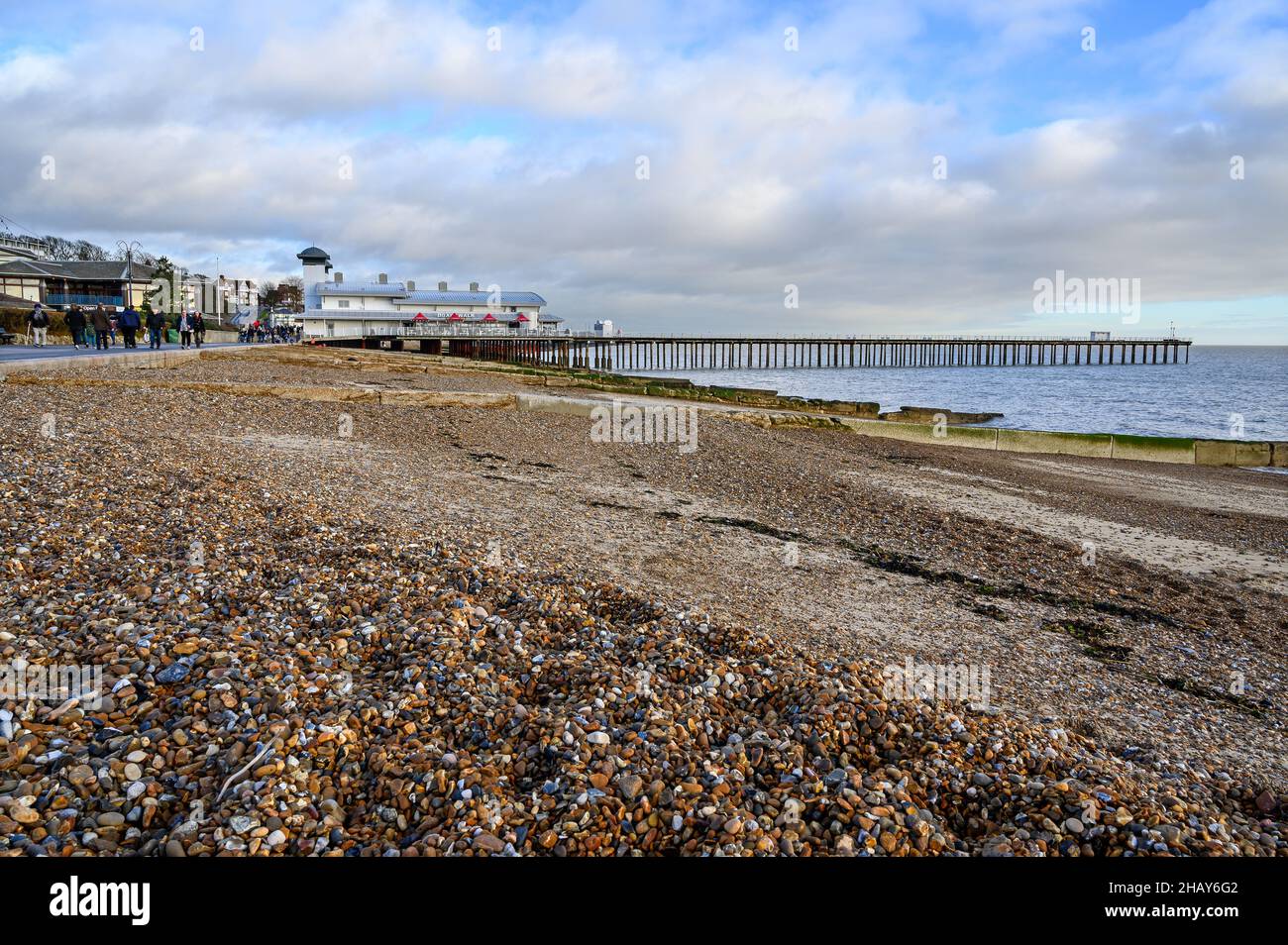 Felixstowe, Suffolk, Großbritannien: Blick auf den Pier von Felixstowe vom Kiesstrand aus. Die Leute laufen entlang der Promenade. Stockfoto