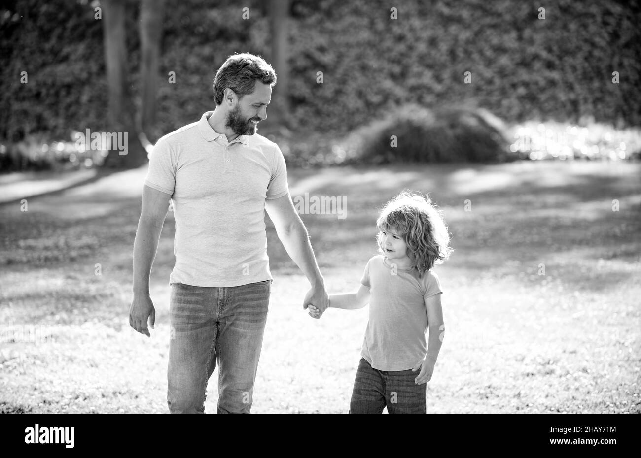 Glücklicher Sohn und Vater halten die Hände zu Fuß an sonnigen Sommertag im Park Gras, Vaterschaft Stockfoto