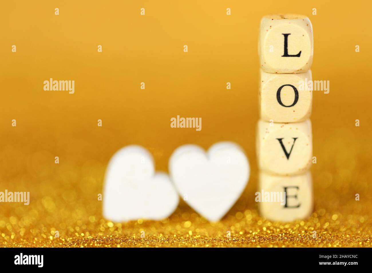 Liebe und Beziehung.Valentinstag. Inschrift Love aus Holzbuchstaben und weißen Herzen auf einem glitzernden Hintergrund mit goldenem Bokeh. Valentinstag Stockfoto