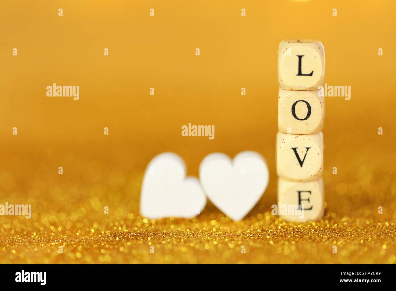 Liebe und Beziehung.Valentinstag. Inschrift Love aus Holzbuchstaben und weißen Herzen auf goldenem Glitzer-Hintergrund mit goldenem Bokeh Stockfoto