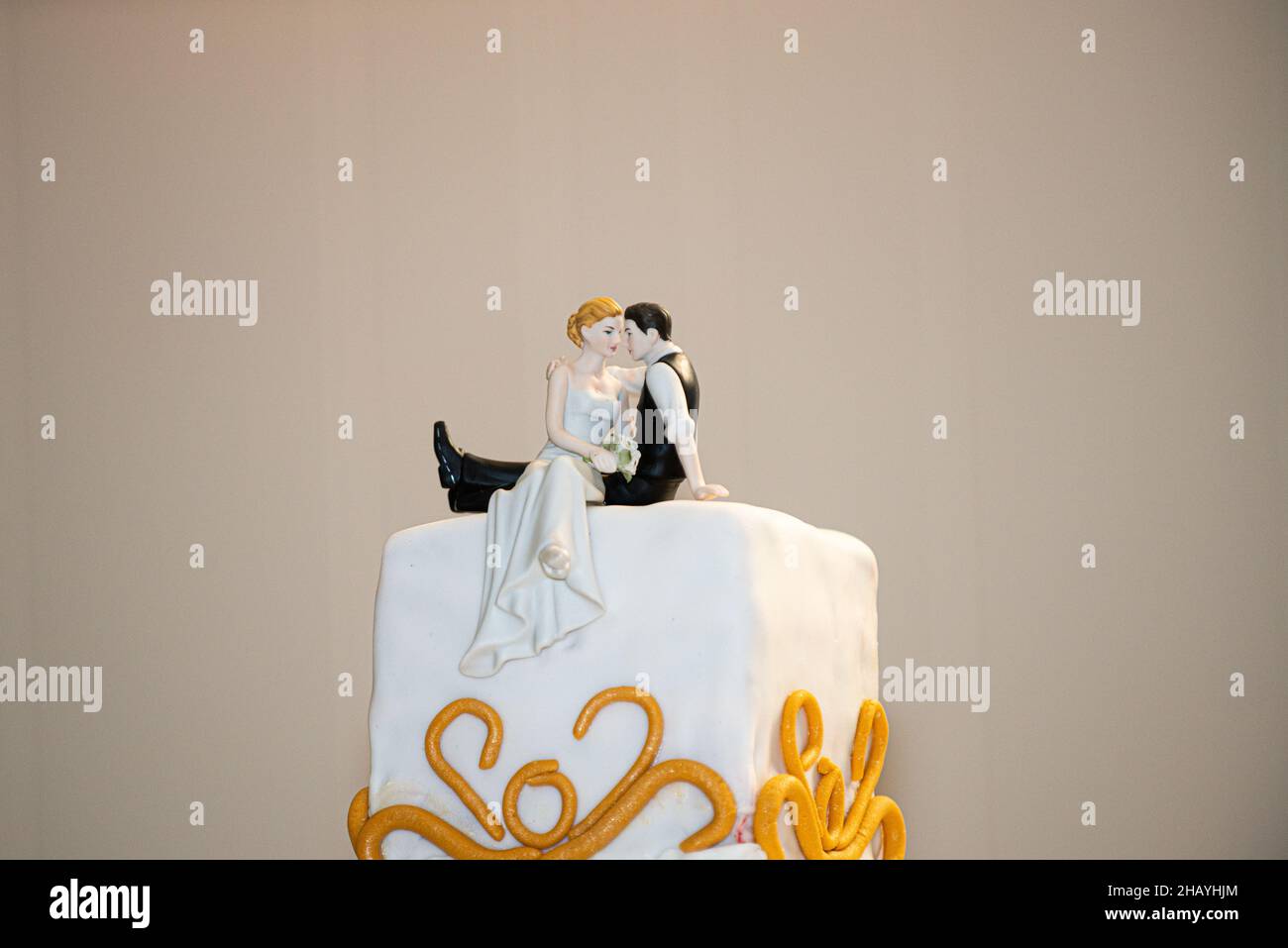 Wundervolle dreistöckige Hochzeitstorte mit goldenem Fondant-Dekor und Braut- und Bräutigam-Tortenauflage Stockfoto