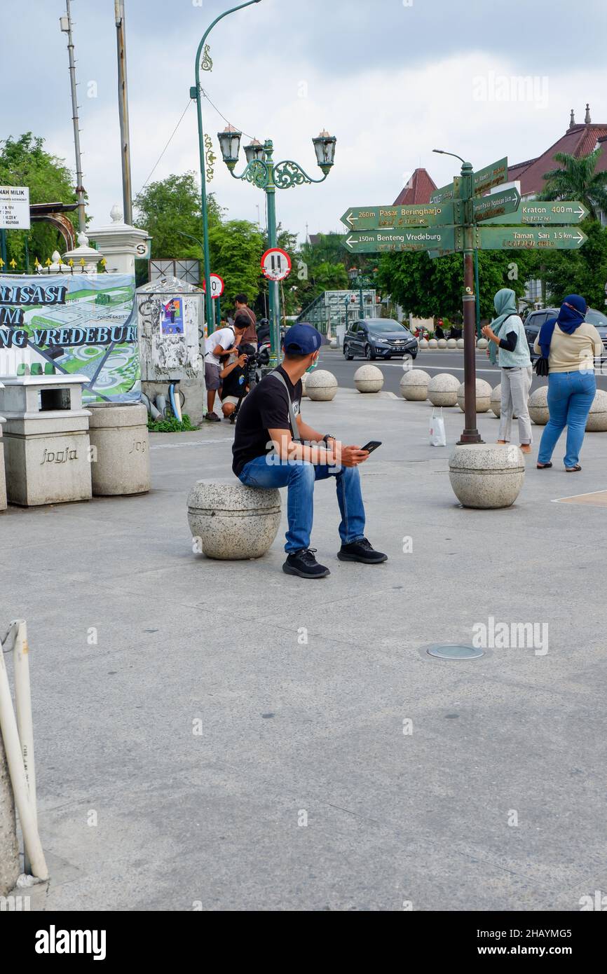 yogyakarta, Indonesien - November 20 2021 : Männer sitzen tagsüber auf Sitzplätzen im Stadtzentrum, während sie Handys spielen Stockfoto