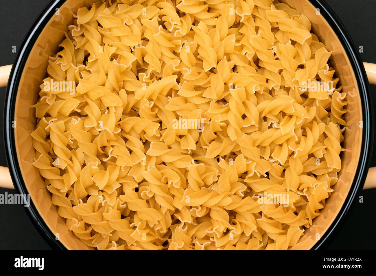 Ungekochte Fusilli Pasta im Metalltopf auf schwarzem Hintergrund. Rohe und trockene Macaroni. Ungesunde und fettarme Lebensmittel. Italienische Kultur Stockfoto