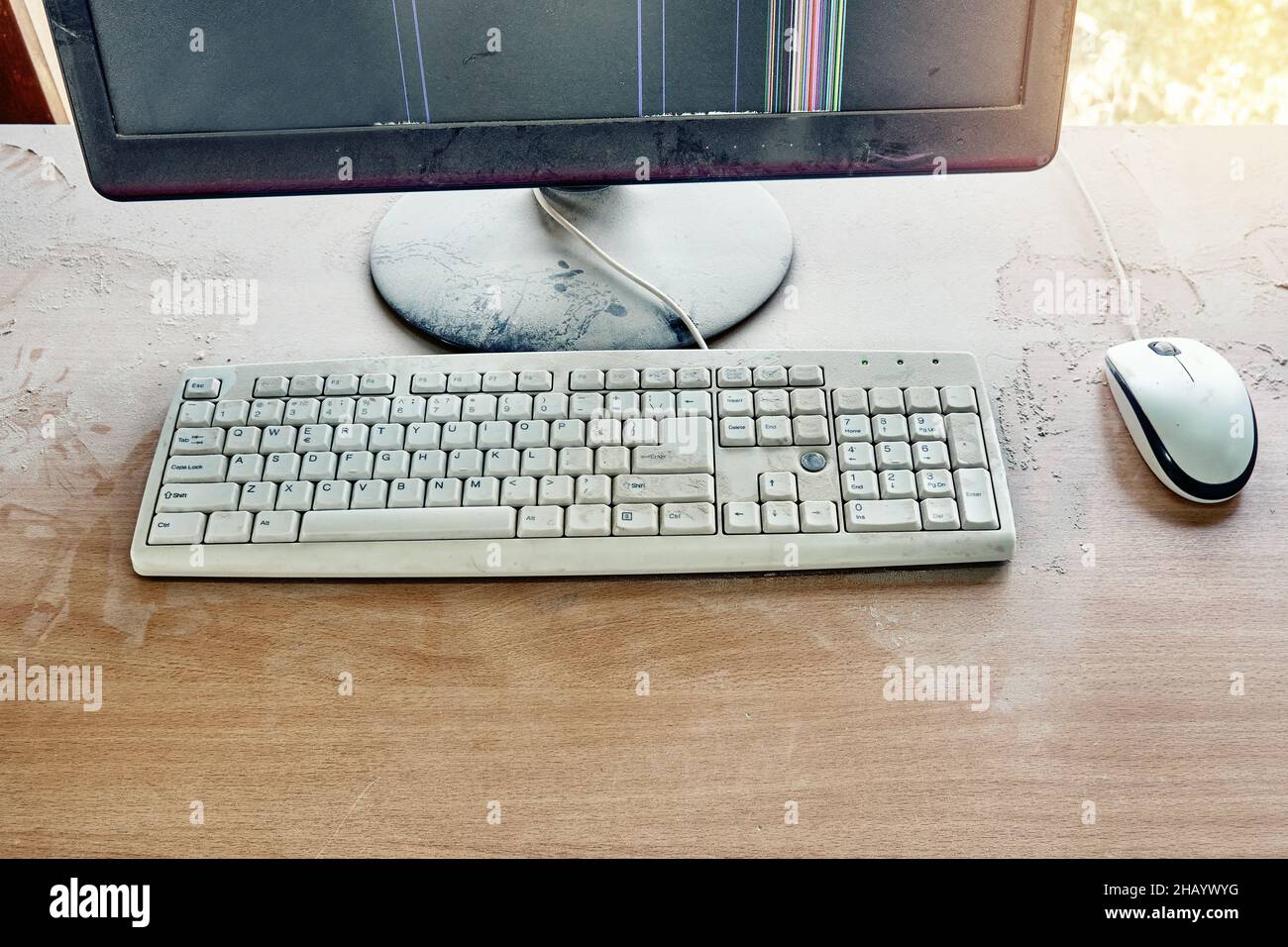 Alte Tastatur mit Maus und kaputtem Monitor stehen auf einem Holztisch und sind in einer Werkstatt mit dickem Staub bedeckt. Draufsicht Stockfoto