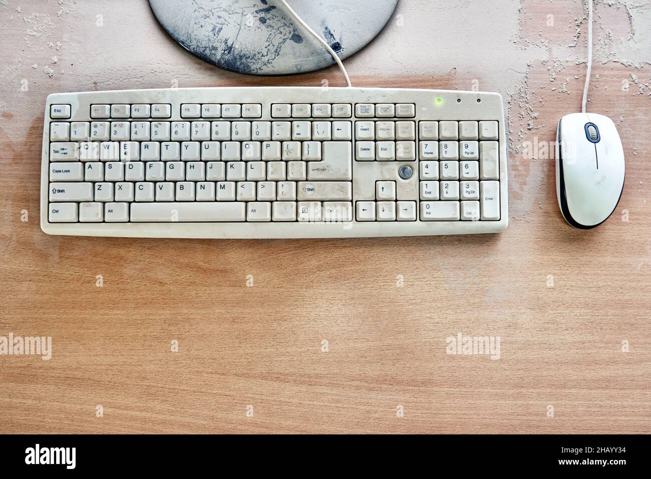 Alte Tastatur mit Maus und kaputtem Monitor stehen auf einem Holztisch und sind in einer Werkstatt mit dickem Staub bedeckt. Draufsicht Stockfoto