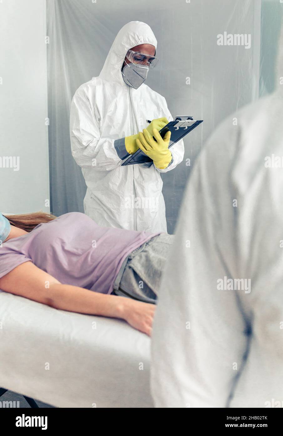 Ärzte in bakteriologischem Schutz, die einen Patienten auf einer Liege medizinisch untersuchen Stockfoto