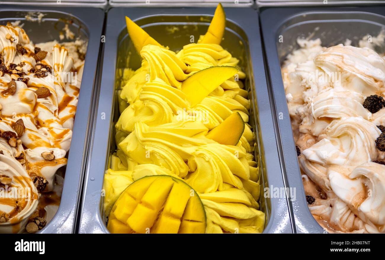 Mango-Eis mit Fruchtstücken von oben. Verschiedene Eiscreme in Tabletts in der Eisdiele. Stockfoto