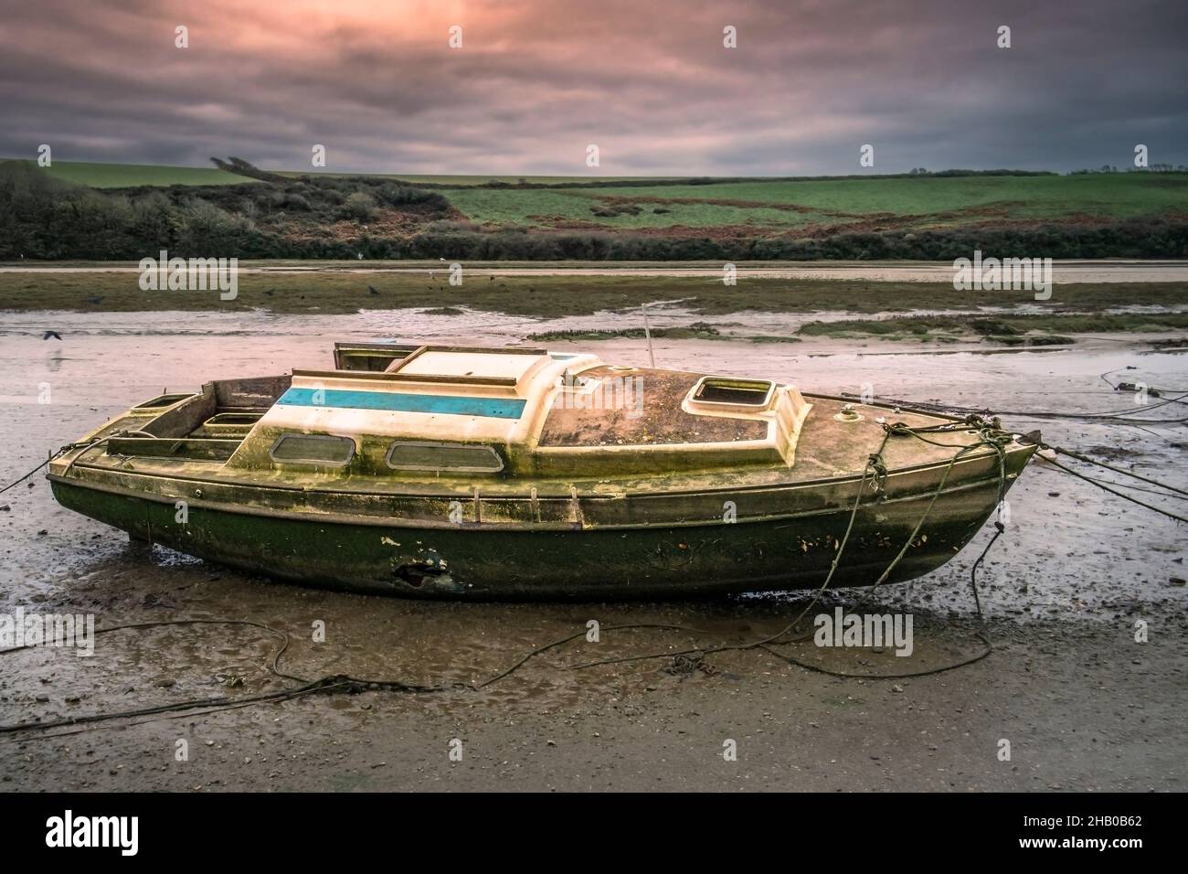 Abendlicht über den Überresten eines alten Segelbootes, das am Ufer des Gannel River in Newquay in Cornwall festgebunden und verlassen wurde. Stockfoto