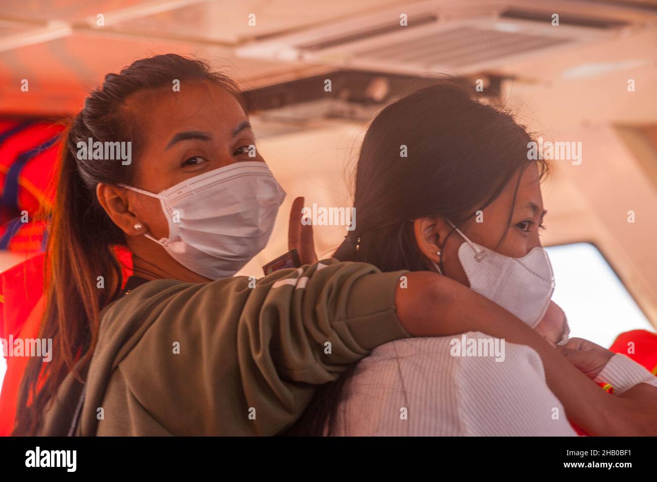 2 Frauen, inländische Touristen, (1 Kambodschaner, links, 1 gemischte Rassen, Rechts, 1/4 Vietnamesen, 1/4 Cham, 1/4 Chinesen und 1/4 Kambodschaner), mit schützenden Gesichtsmasken, fahren Sie mit der Fähre nach Saracen Bay, Koh Rong Samloem während der COVID - Pandemie 19. Golf von Thailand, Provinz Sihanoukville, Kambodscha. 6th. Dezember 2021. © Kraig Lieb Stockfoto