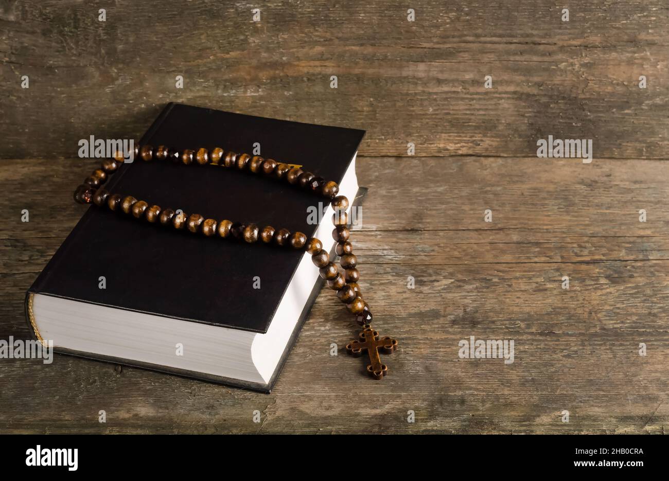 Bibel mit Rosenkranz auf altem Holzhintergrund mit Kopierraum, Religionskonzept mit Filmkorneffekt Stockfoto