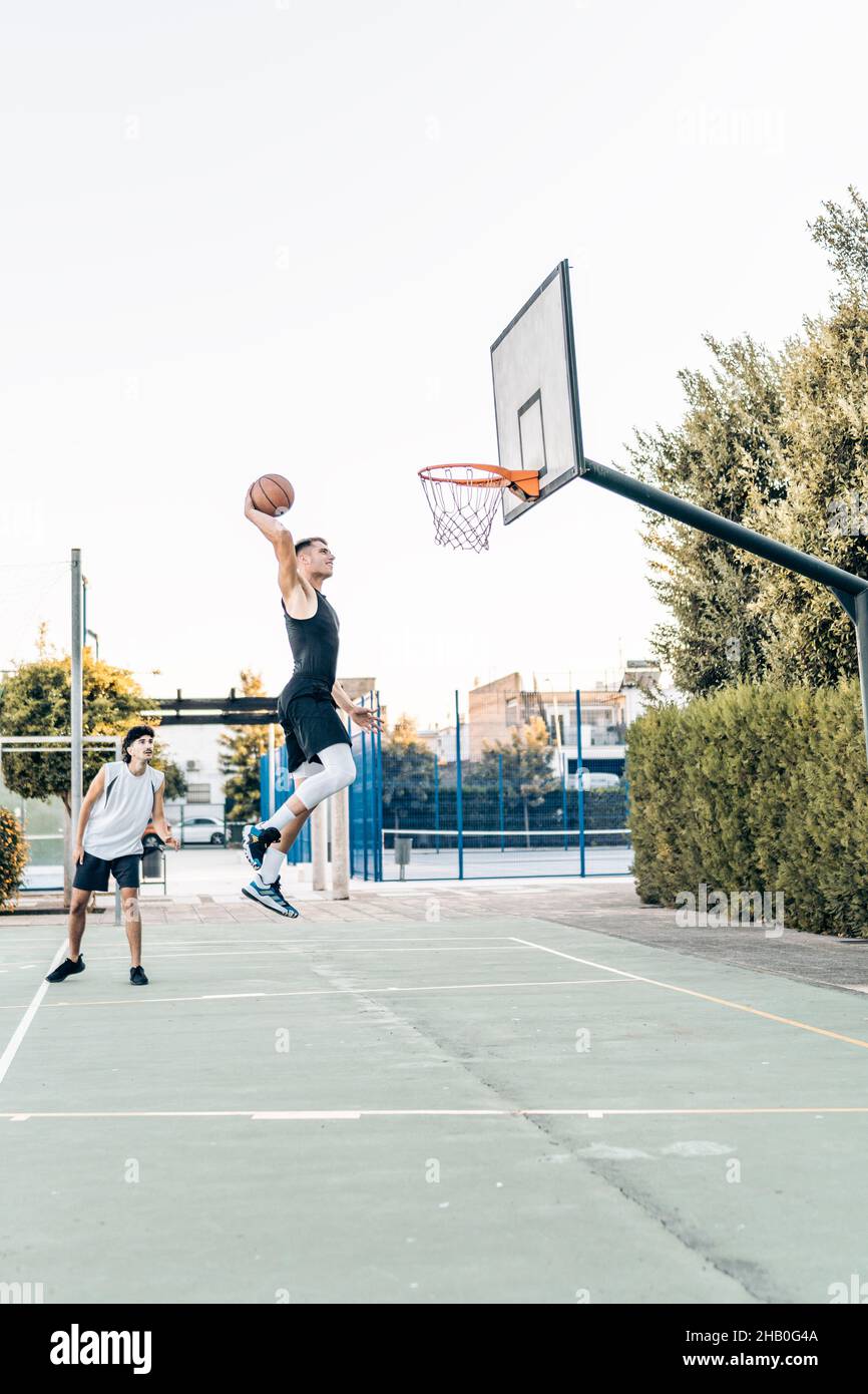 Vertikales Foto eines Mannes, der beim Scoring während eines freundlichen Basketballspiels springt Stockfoto